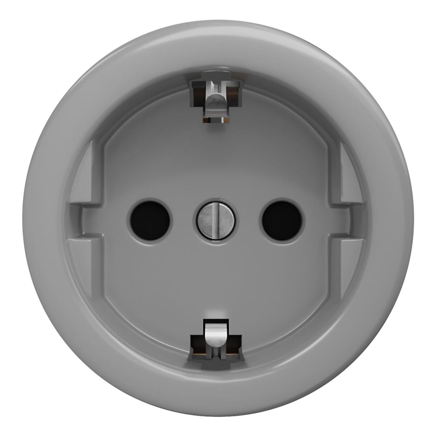 Šedá elektrická zásuvka s dvoma otvormi a uzemnením je umiestnená na bielom pozadí. Zásuvka je okrúhleho tvaru s plochým povrchom.