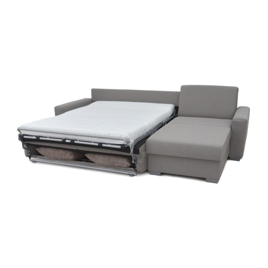 Rohová sedačka sivej farby stojí na bielom pozadí. Sedačka je rozkladacia a má tri samostatné sedáky. Jej súčasťou je aj široká podnožka.