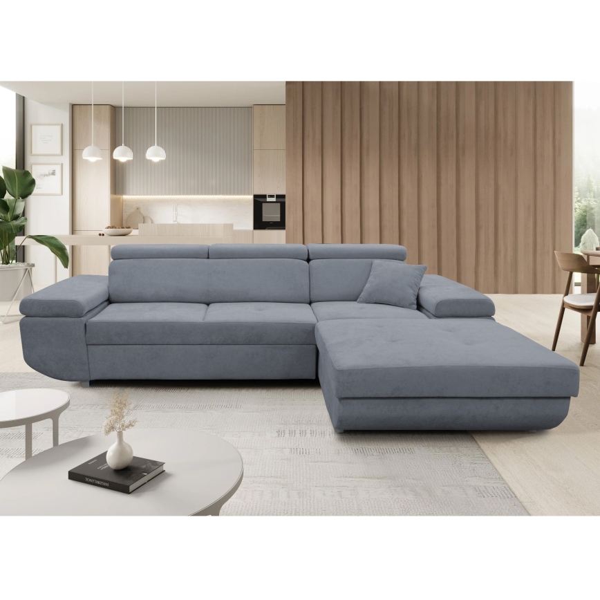 Rohová sedačka sivomodrej farby je umiestnená na bielom pozadí. Sedačka má tri časti: dve dlhšie a jednu menšiu, ktorá tvorí roh. Na jednej časti je opierkový vankúš.