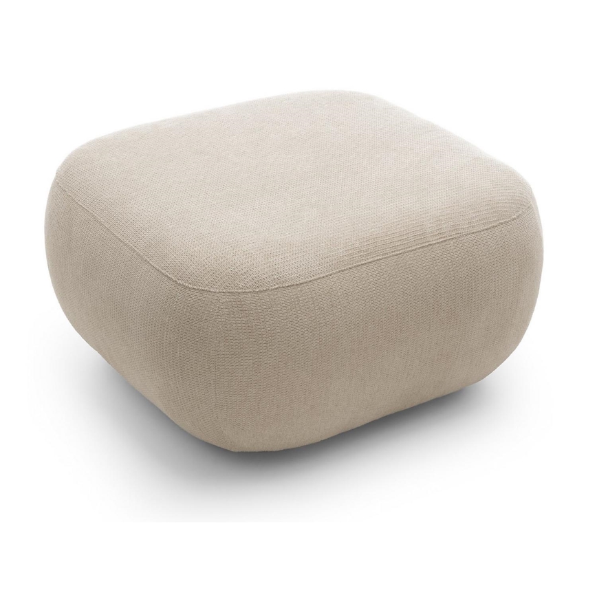 Priestranný čalúnený taburet svetlohnedého odtieňa s oblými tvarmi stojí na bielom pozadí.