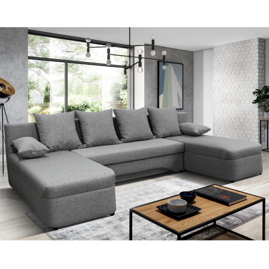 Rohová sedačka s rozkladacím mechanizmom, sivá látková poťahová látka, štyri operadlové vankúše a jeden malý vankúš. Sedačka je umiestnená na bielom pozadí.